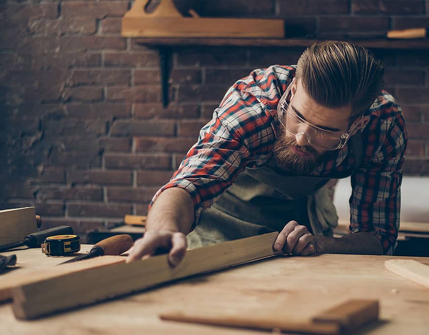 Mann mit Schutzbrille bearbeitet eine Holzbohle